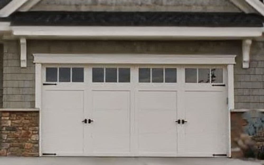 White garage door with decorative windows and stone accents, modern home exterior.