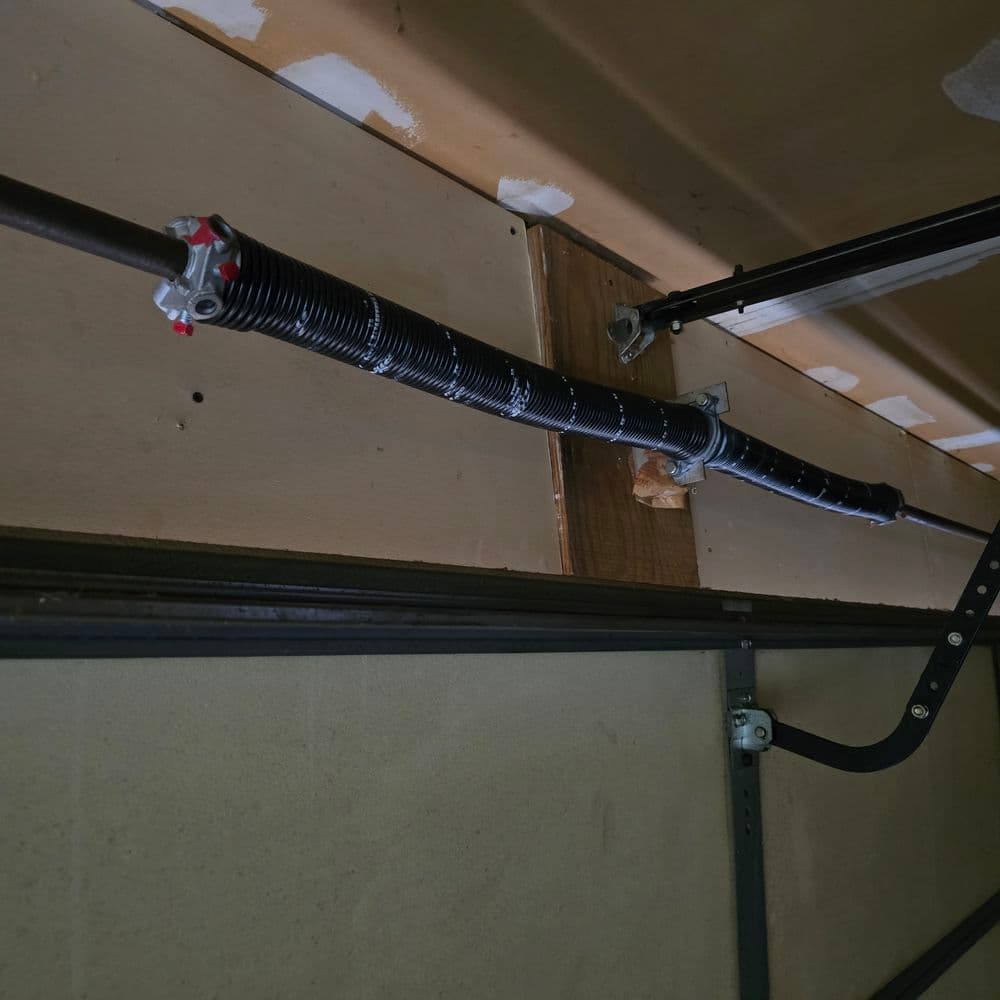 Garage door torsion spring system installed on the wall, with black wrapping and hardware visible.