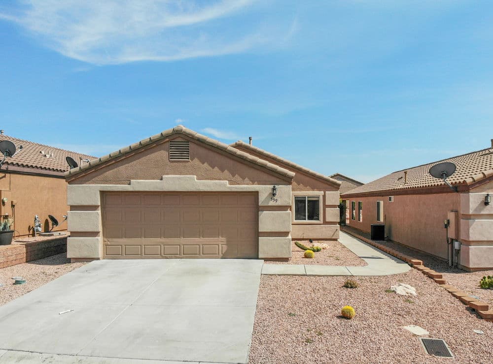 Single-story beige home with a garage, landscaped front yard, and clear blue sky.