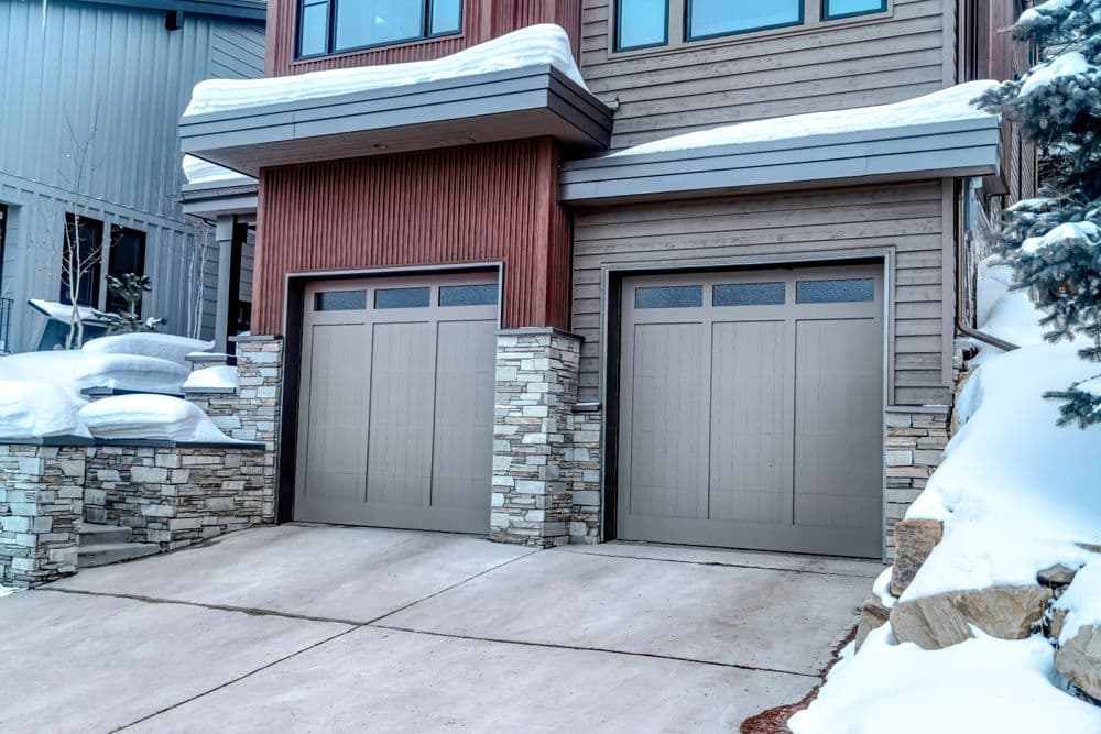 Modern home with stone accents and two gray garage doors in a snowy landscape.