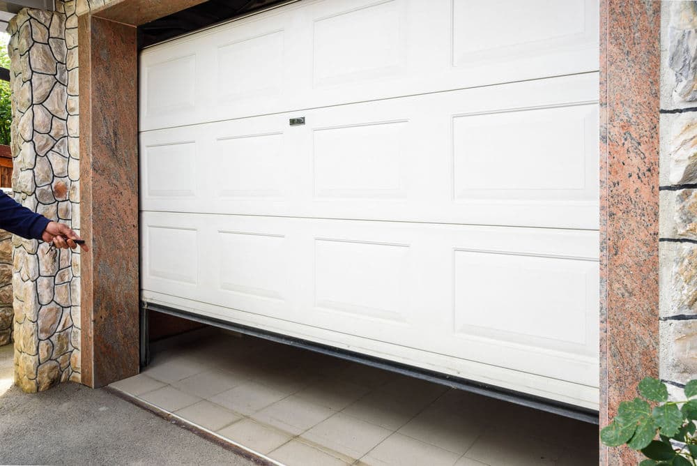 White garage door opening with remote control in hand, showcasing modern home entry.