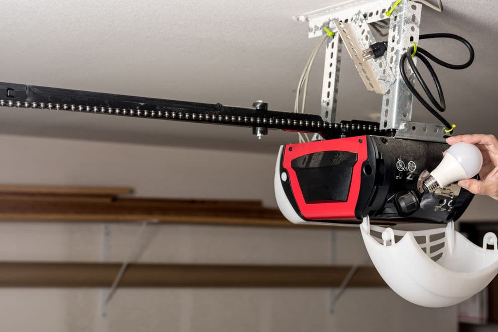 Garage door opener with red and black design, mounted on ceiling with chain drive mechanism.