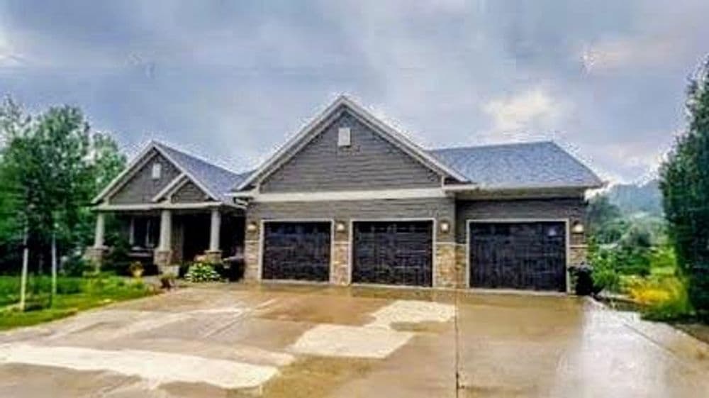 Modern gray house with three-car garage, lush landscaping, and cloudy sky backdrop.