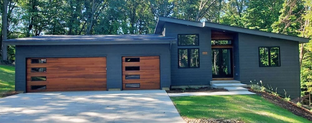 Modern dark gray house with wooden garage doors and a landscaped front yard.